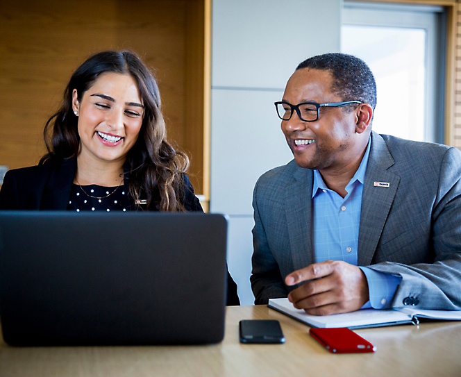 Muž a žena se usmívají a diskutují, zatímco pracují na jejím přenosném počítači