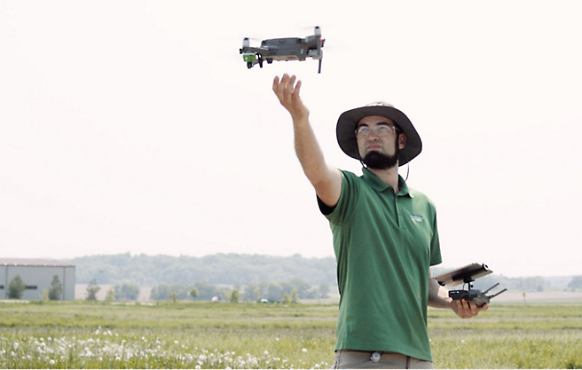 Een man laat een drone in een veld vliegen.