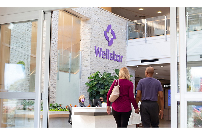 Two people walking in front of a wellstar building.