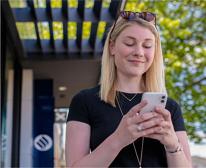 A woman smiling while using her phone with both hands