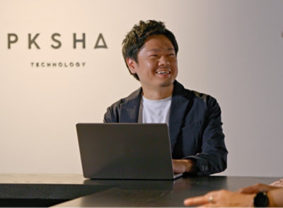 Een glimlachende man met een laptop met de tekst 'PKSHA TECHNOLOGY'.