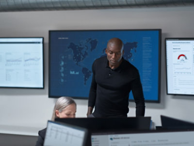 Person standing in a control room with dashboard screens in the background.