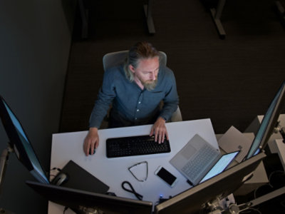 A person sitting at a desk typing on a keyboard with a laptop on the table.