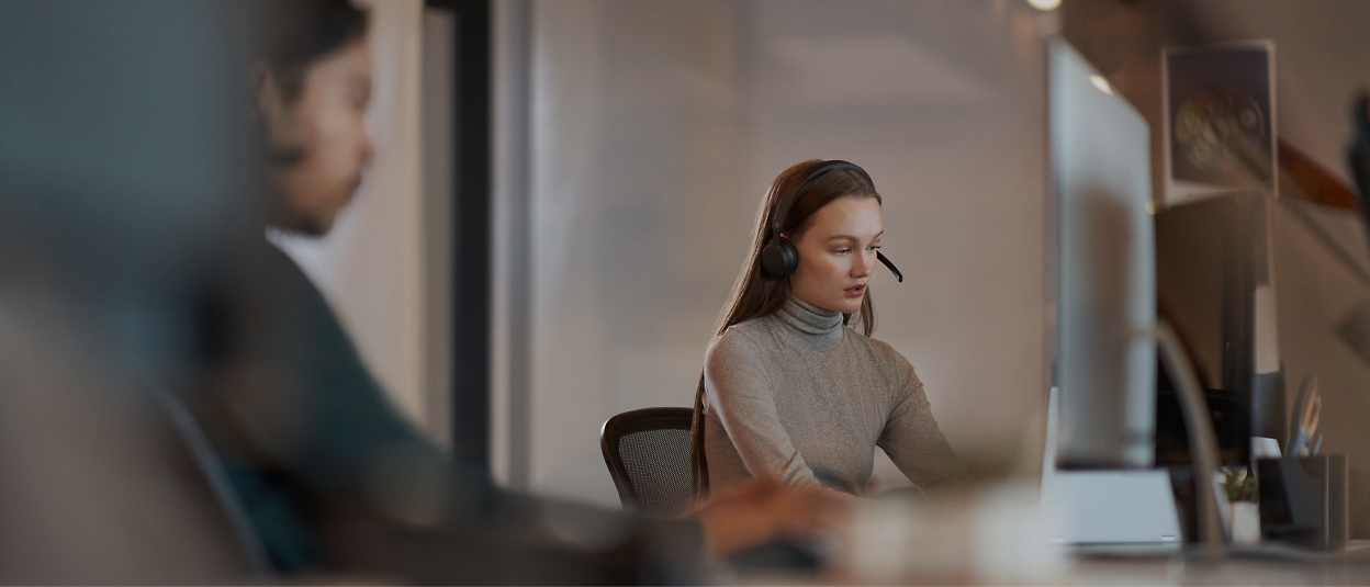 صورة امرأة ترتدي سماعة رأس أثناء العمل على كمبيوتر.