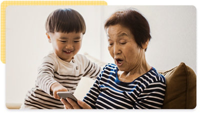 A smiling toddler and older woman sit together looking at something on a phone screen