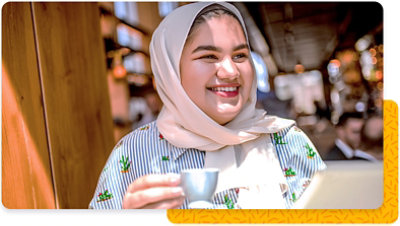 A smiling woman in a sunny cafe, holding a small coffee cup
