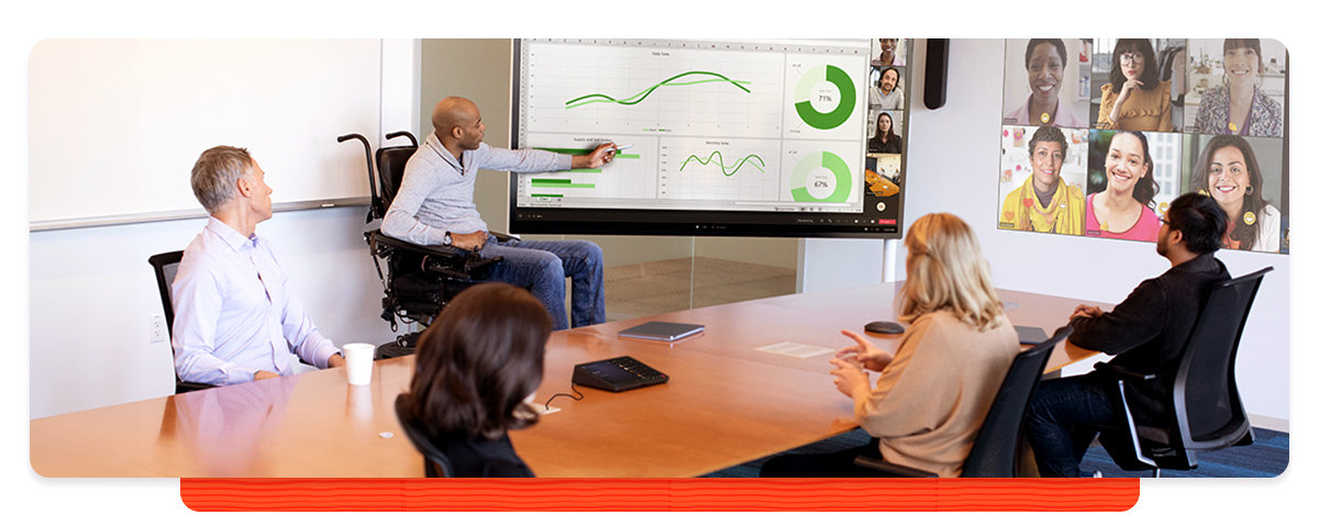 Man using a wheelchair leads a presentation to colleagues in a conference room and in a video call