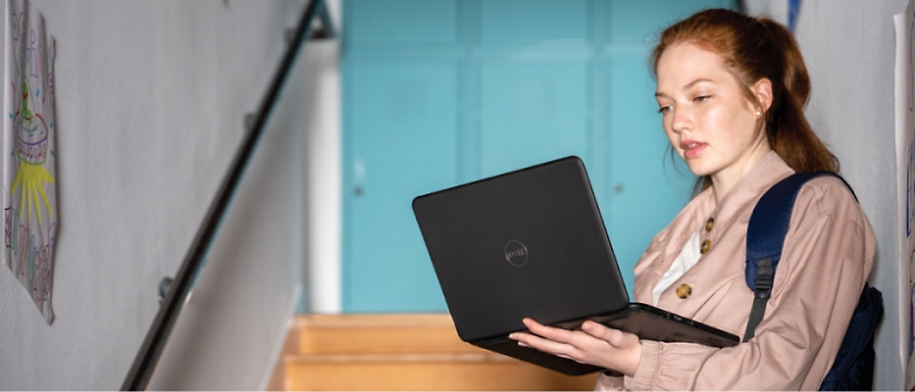 Egy fiatal hátizsákos nő egy laptopot tart a kezében.