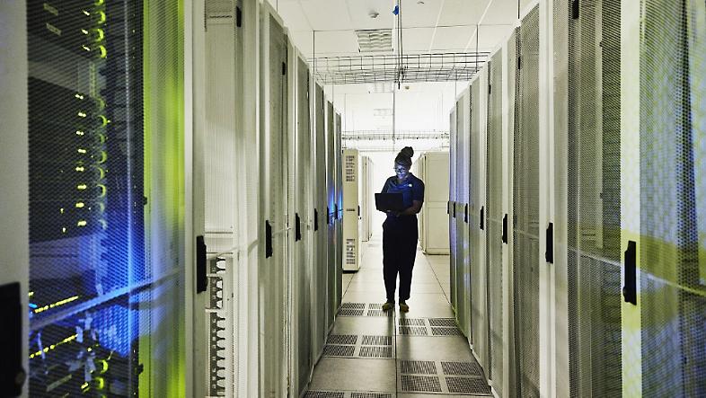 Una persona in piedi in un data center che tiene in mano un portatile.