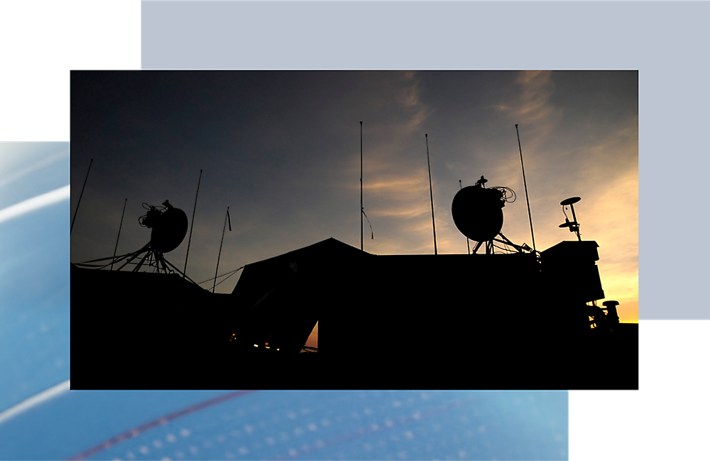 Silhouette d’antennes de communication sur un toit sur un ciel de coucher de soleil avec des teintes orange et bleues éclatantes.