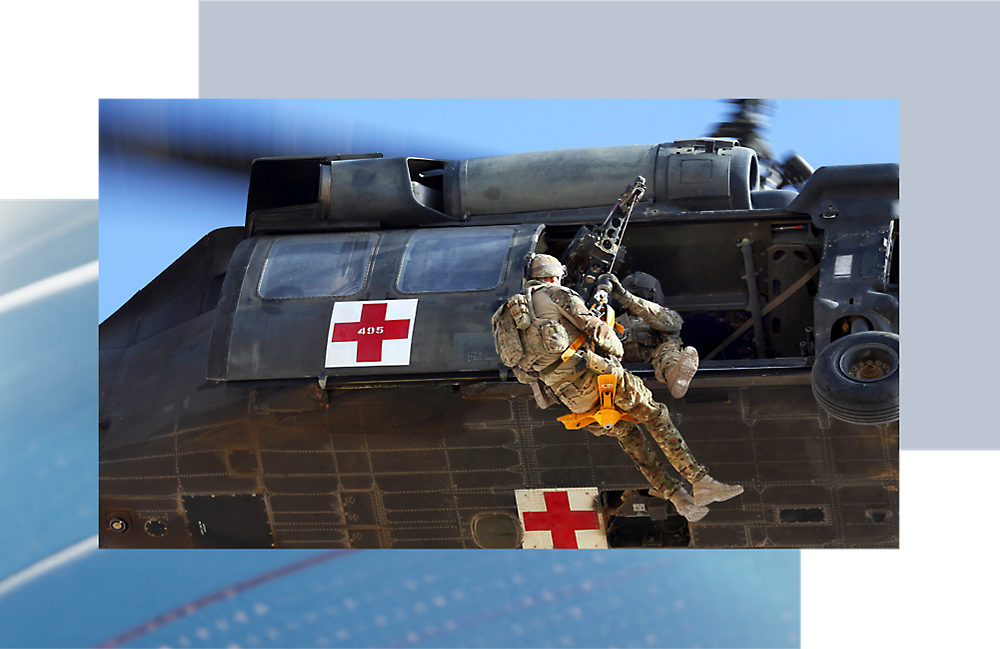 A soldier in camouflage rappels from a black hawk helicopter marked with a red cross 