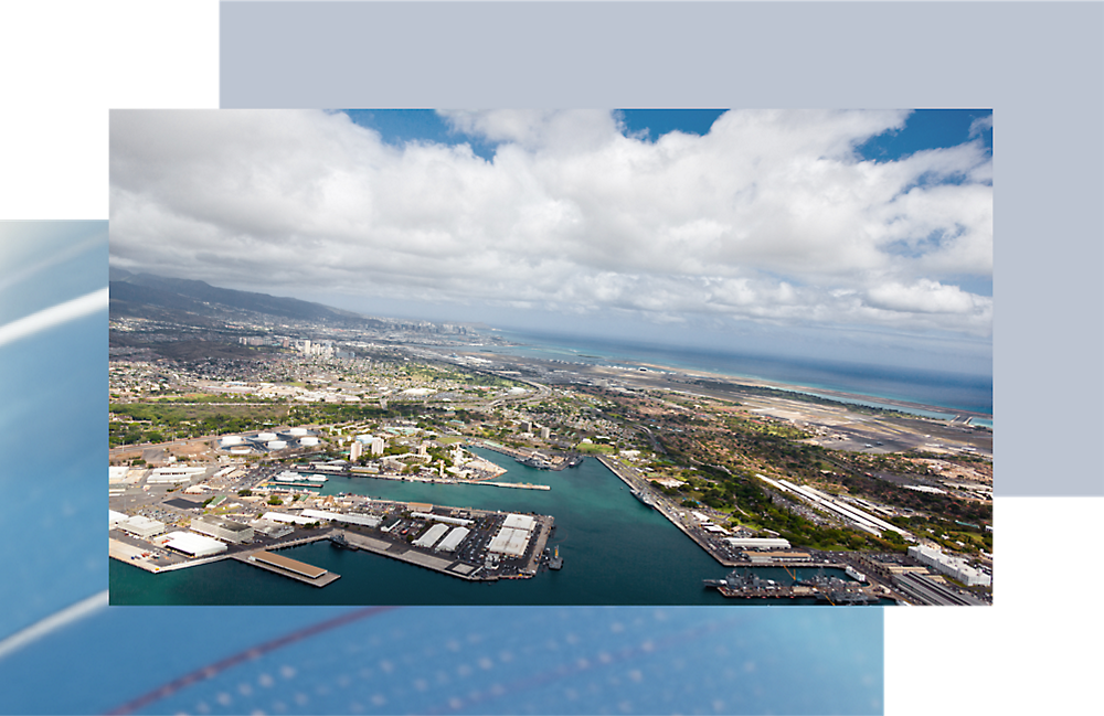 Vista aérea de uma cidade costeira com um porto industrial e um horizonte urbano denso sob um céu parcialmente nublado.