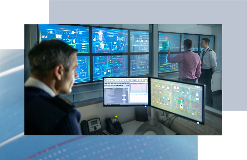 Drei Personen in einem Kontrollraum mit mehreren Bildschirmen, die verschiedene Daten und Karten anzeigen, wobei eine Person aktiv auf einen Bildschirm zeigt.