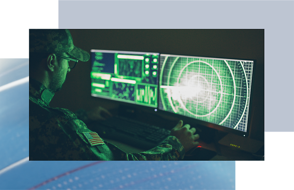 A military personnel in camouflage uniform analyzes data on a multi-screen computer setup displaying radar and digital maps.