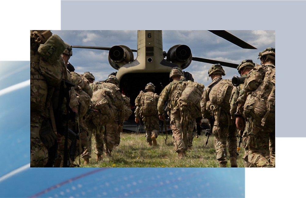 Soldados com equipamento de camuflagem a embarcar num avião de transporte militar num campo relvado sob um céu nublado.