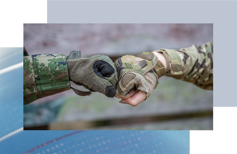 Două persoane în uniforme militare își ciocnesc pumnii, accentul fiind pe mâinile lor cu mănuși.