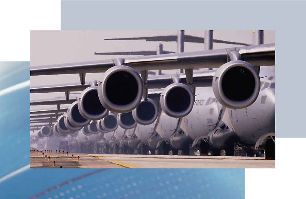 Deretan mesin pesawat besar berjajar di atas aspal, memperlihatkan tampilan depannya dengan latar belakang langit biru yang cerah.