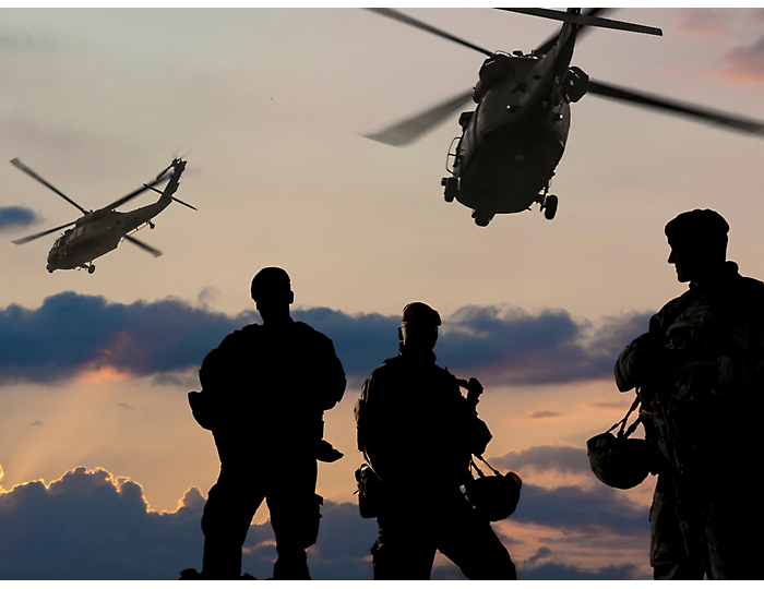 Soldados e helicópteros em silhueta num céu ao pôr do sol.