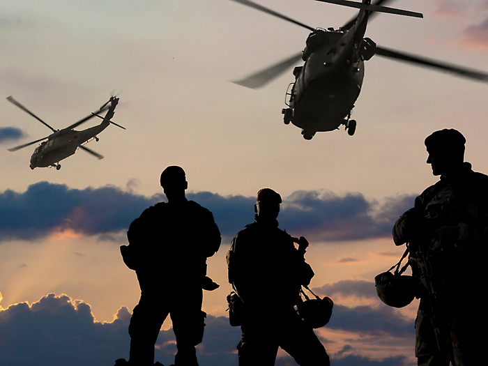 Silhouetted soldiers and helicopters against a sunset sky.