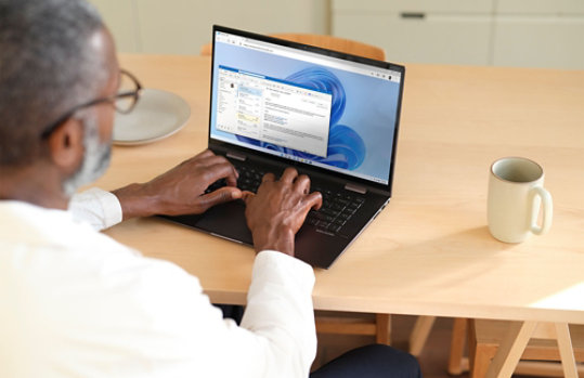 A person using Outlook on a laptop at a kitchen table.