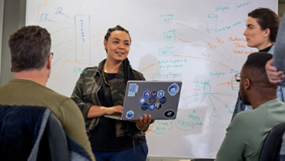 Four people standing around a whiteboard having a standup meeting