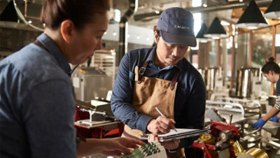 Two people working together while one is writing on a tablet with a pen