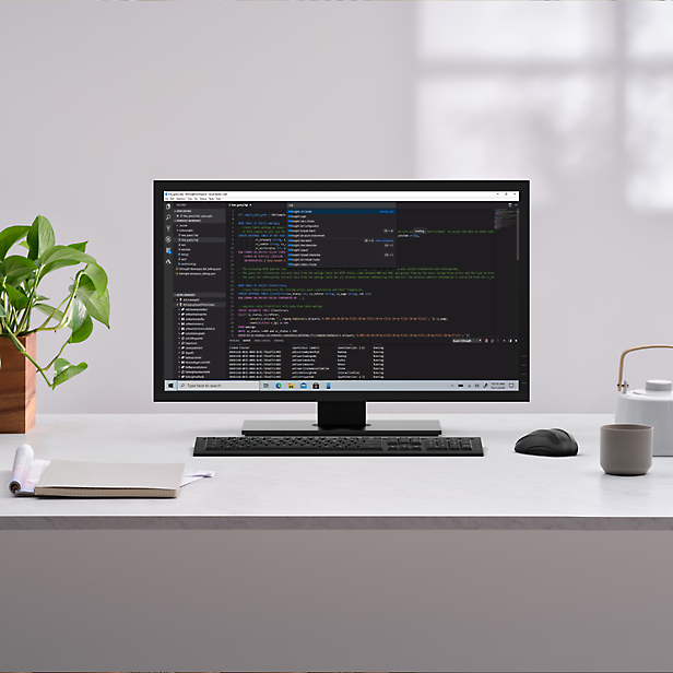 Una scrivania con un monitor con codice scritto in una finestra aperta, una pianta da interno e una tazza di caffè sulla scrivania