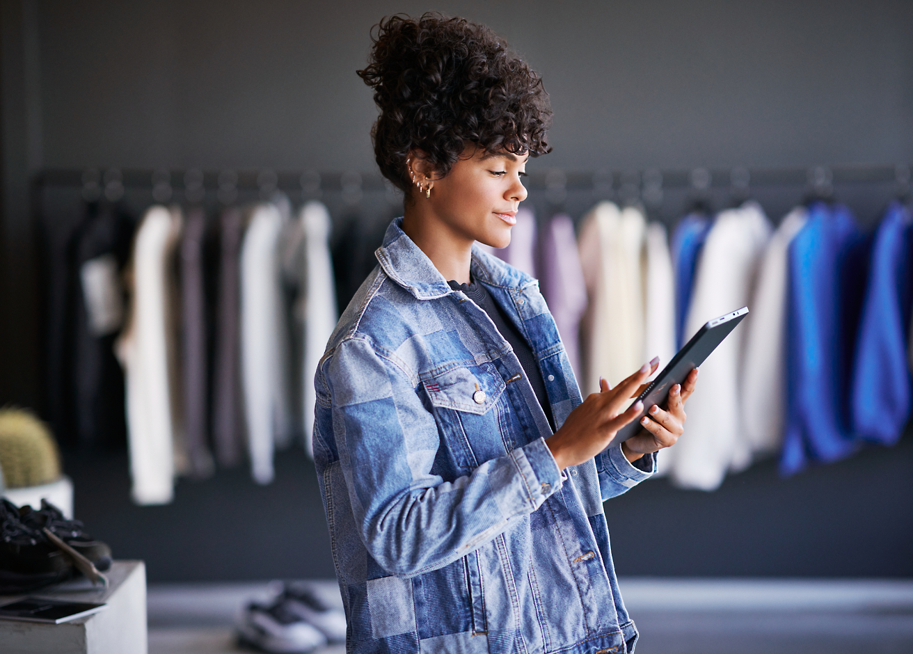 Молодая женщина в джинсовой куртке пользуется планшетом в магазине одежды.