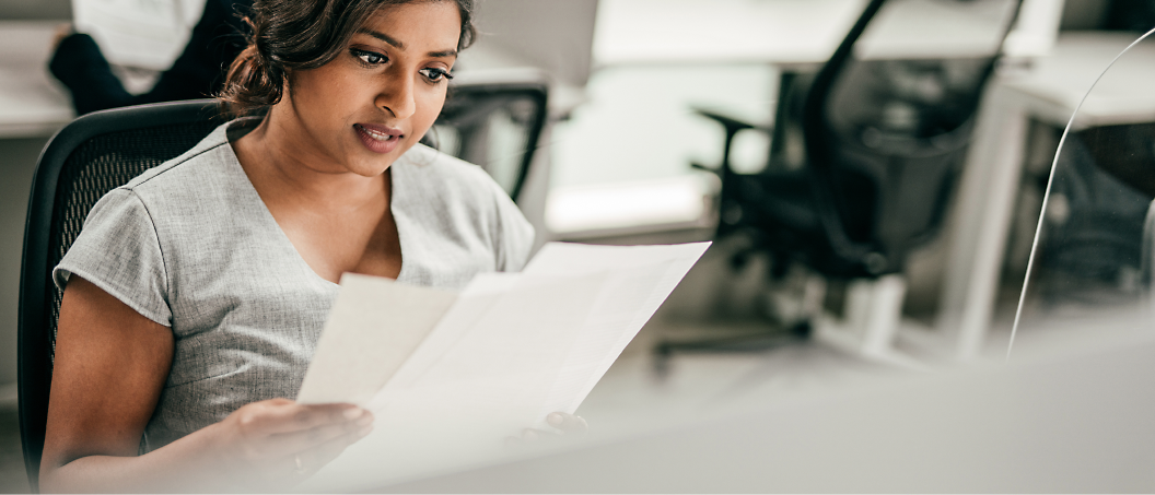 A focused woman reviewing documents at her desk in an office environment.