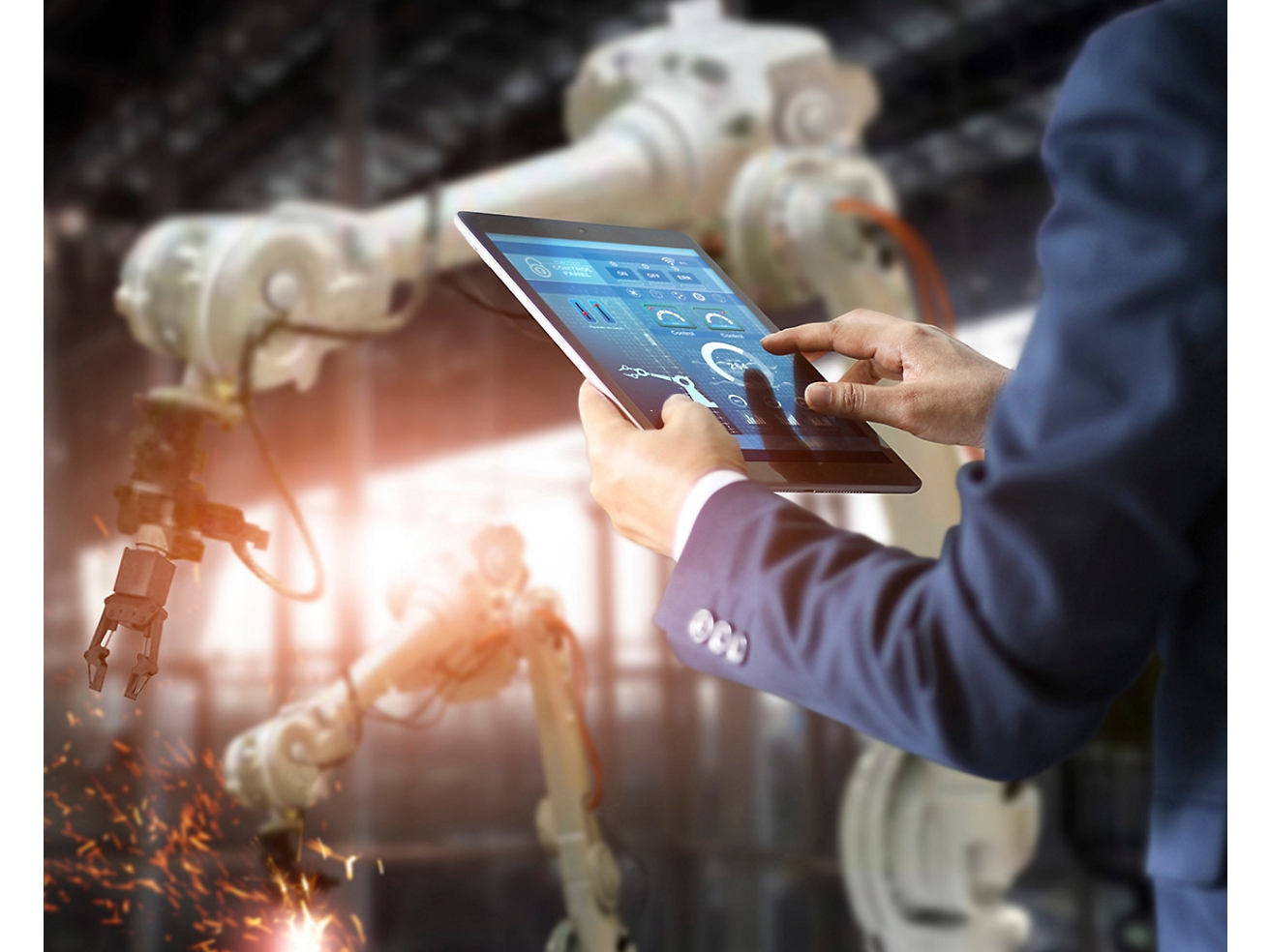 Una persona controla en una fábrica unos brazos robóticos mediante una tableta, lo que pone de relieve la avanzada tecnología de automatización.