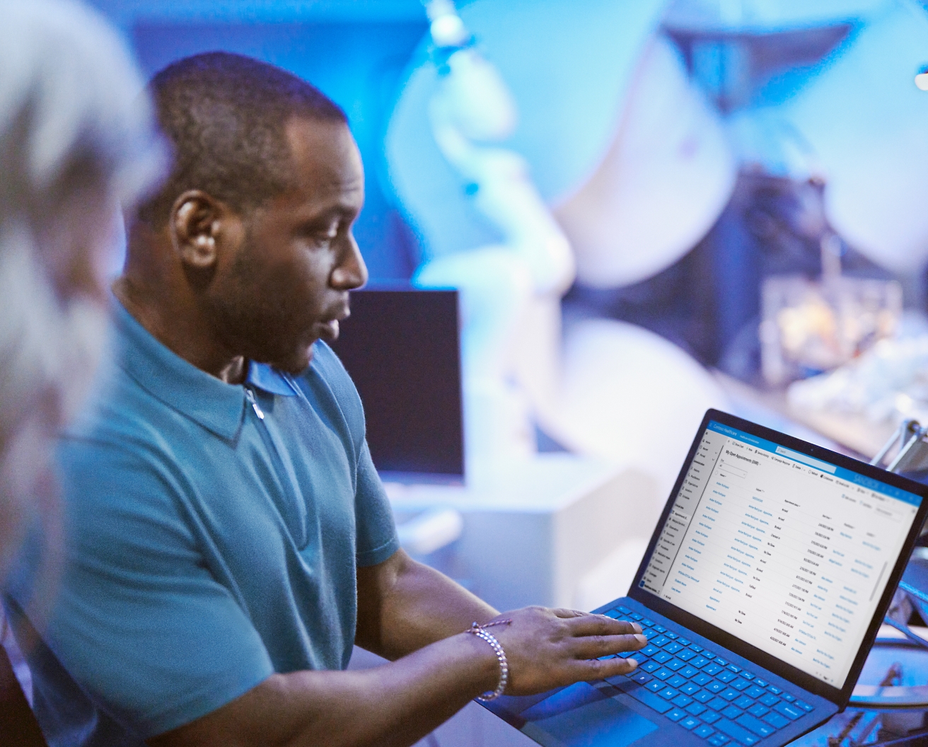 Hombre revisando datos en un portátil en una ajetreada oficina con compañeros a su alrededor.