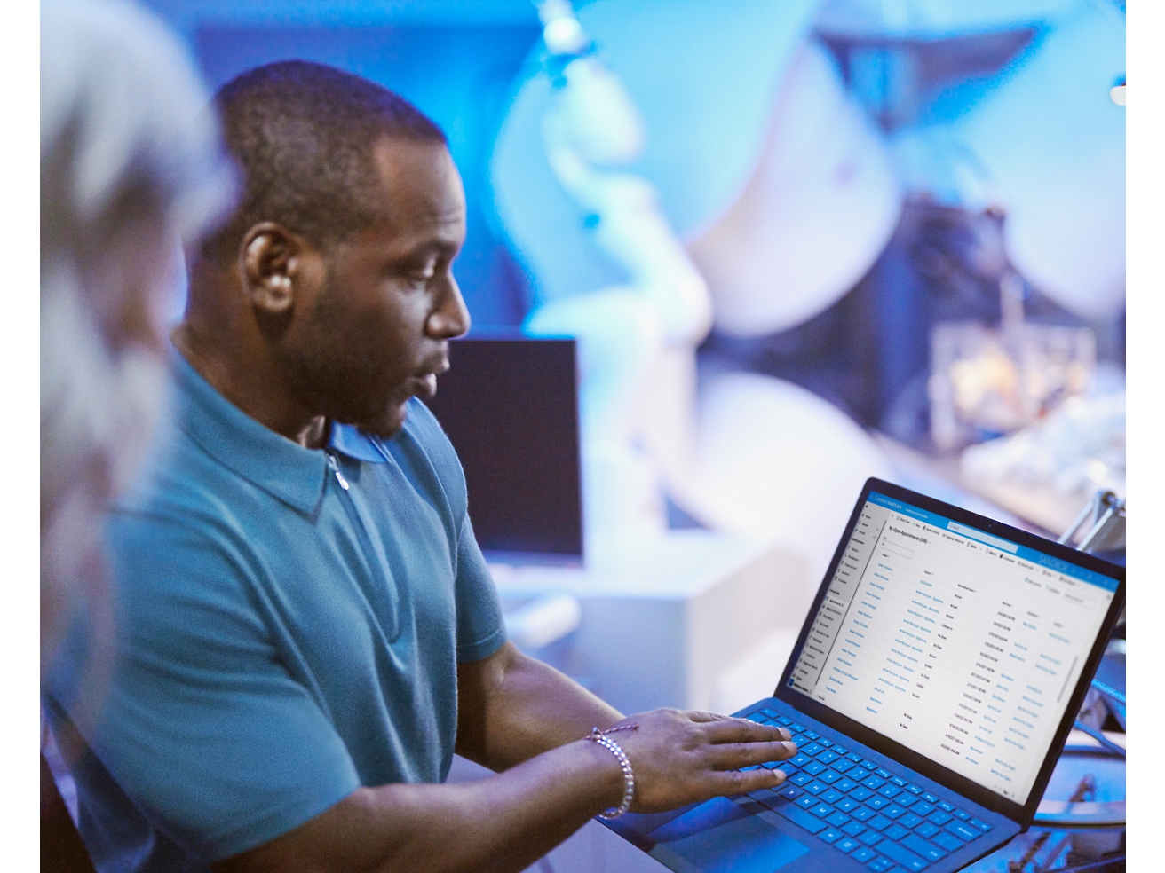 Hombre revisando datos en un portátil en una ajetreada oficina con compañeros a su alrededor.