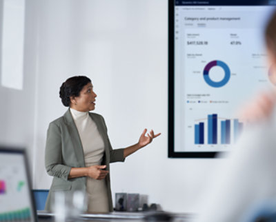 A professional woman presents financial data on a screen to her audience in a modern office setting.