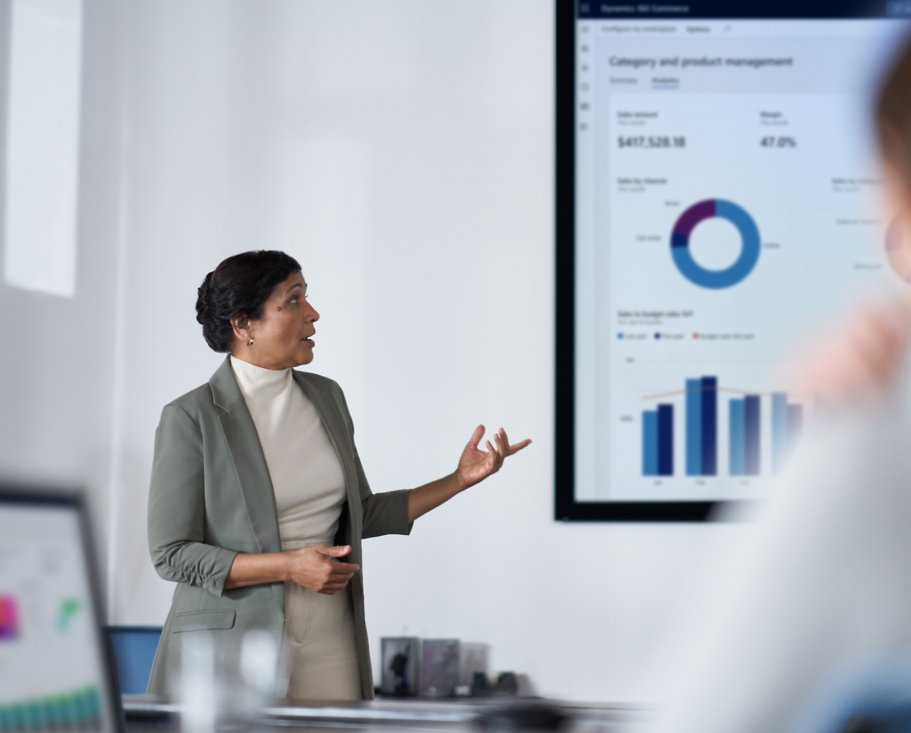En professionel kvinde præsenterer finansielle data på en skærm til sit publikum i et moderne kontorscenarie.