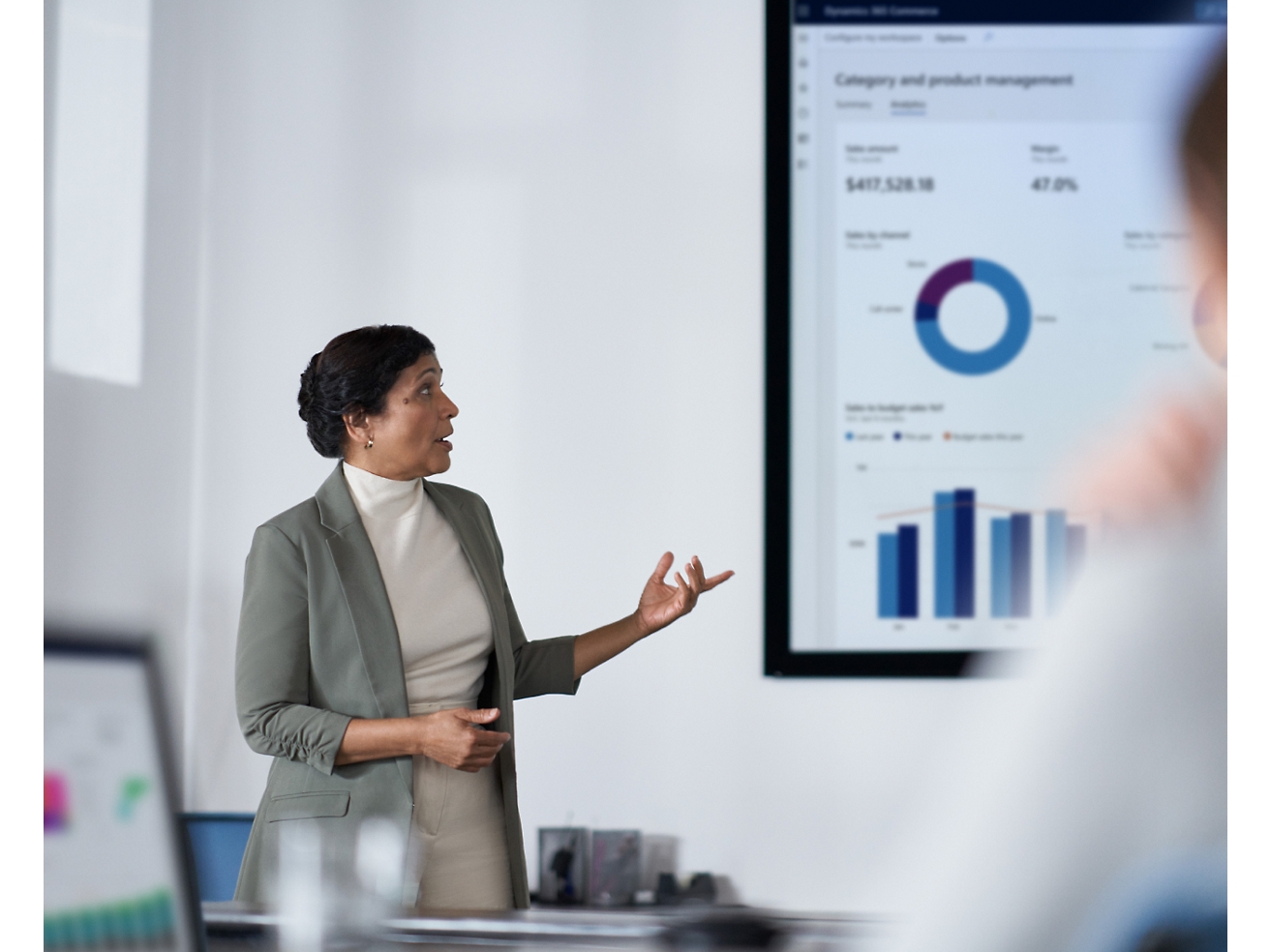 A professional woman presents financial data on a screen to her audience in a modern office setting.