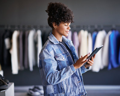 A woman in a denim jacket is using a tablet in a clothing store