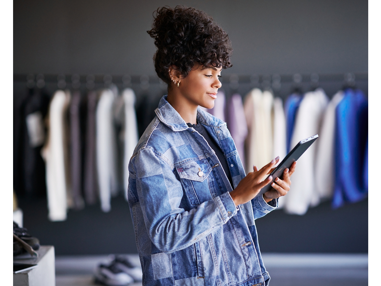Женщина в джинсовой куртке работает на планшете в магазине одежды