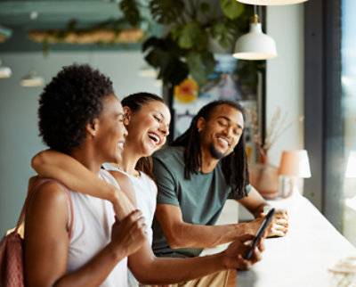 Three friends laughing and looking at a smartphone together in a modern café.