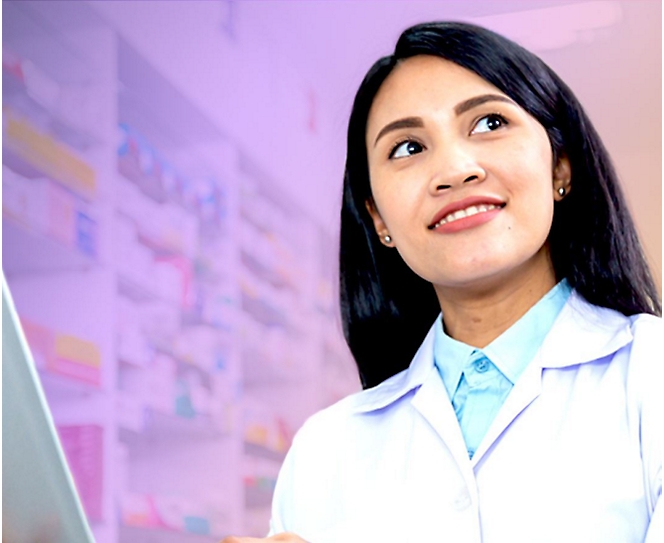 A person wearing a white lab coat is looking up and smiling, with shelves of medical supplies in the blurred background