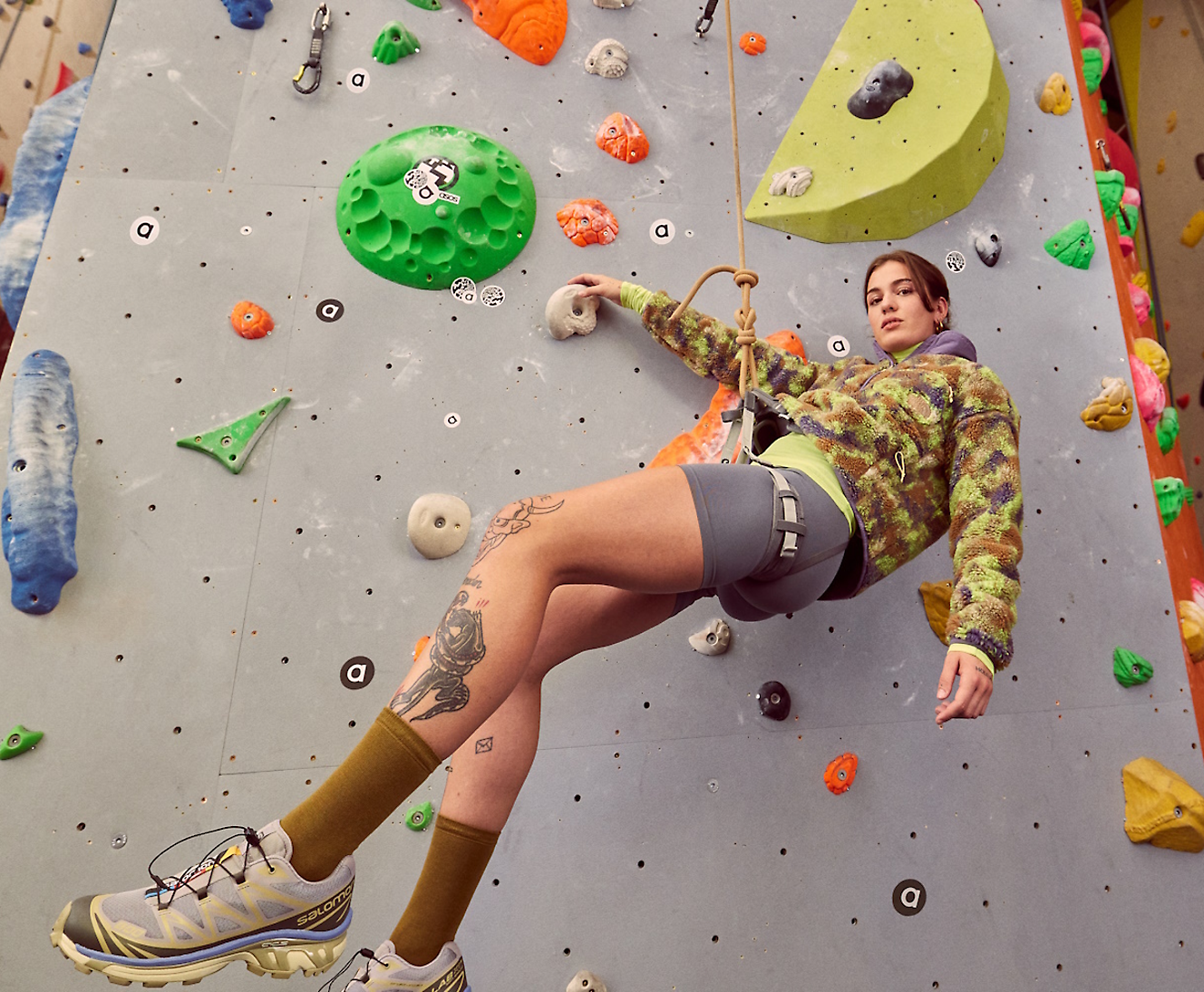 A person wearing climbing gear ascends an indoor rock climbing wall with various colored holds and grips.