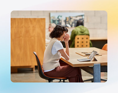 Person som sitter vid ett skrivbord, ler och tittar på en skärm, i ett rum med trämöbel 