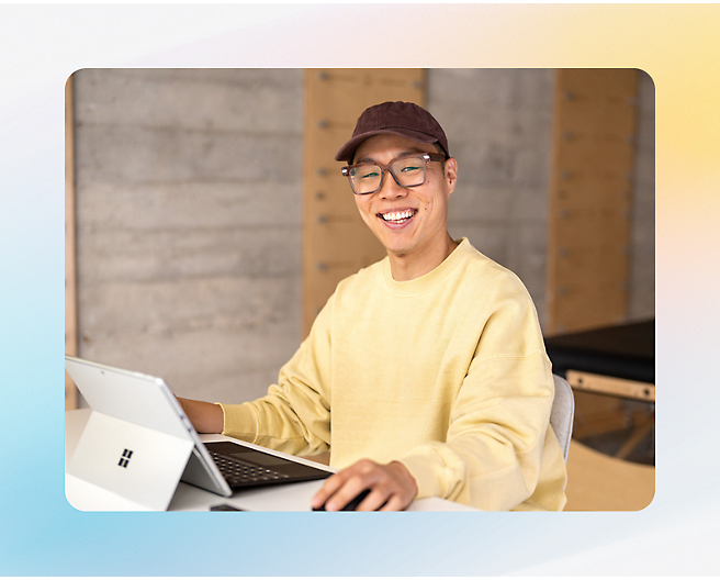 A man wearing a yellow sweater is smiling while using laptop.
