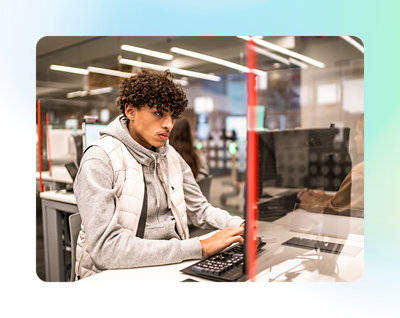 透明なパーティションで区切られたモダンなオフィス、または学習スペースでコンピューターがあるデスクに座っている人物。