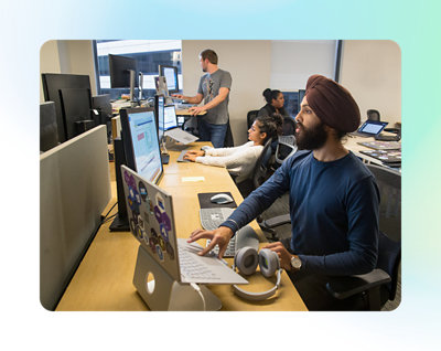 オフィスのコンピューター デスクで仕事をしている 4 人の人物。各自が自分のコンピューターの画面に集中している。