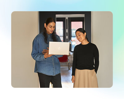 廊下に立ってノート PC を見ている 2 人の人物。どちらも笑顔で、カジュアルな服を着ている。