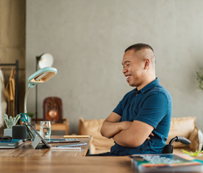Man smiling at digital tablet on desk in a warmly lit home office.