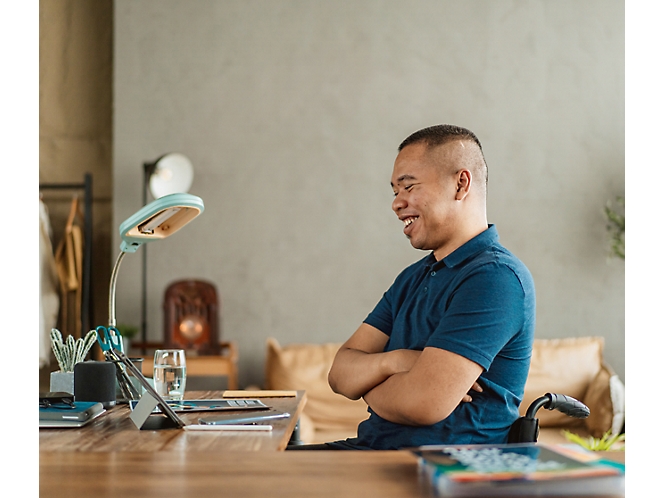 Homem sorrindo para um tablet digital na mesa em um escritório doméstico bem iluminado.