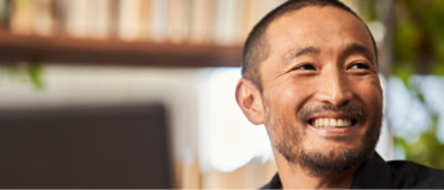 En man med kort hår och nära beskuret hår ler medan han tittar åt vänster, med hyllor 