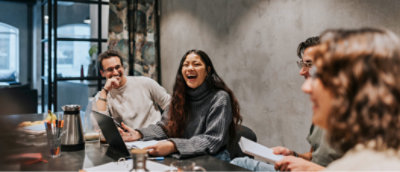 Een diverse groep van vier personen zit rondom een tafel in een modern kantoor, bezig met een vergadering.