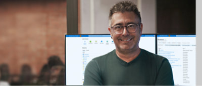 眼鏡をかけてひげを生やしている男性が、笑顔でコンピューター画面の前に立っている